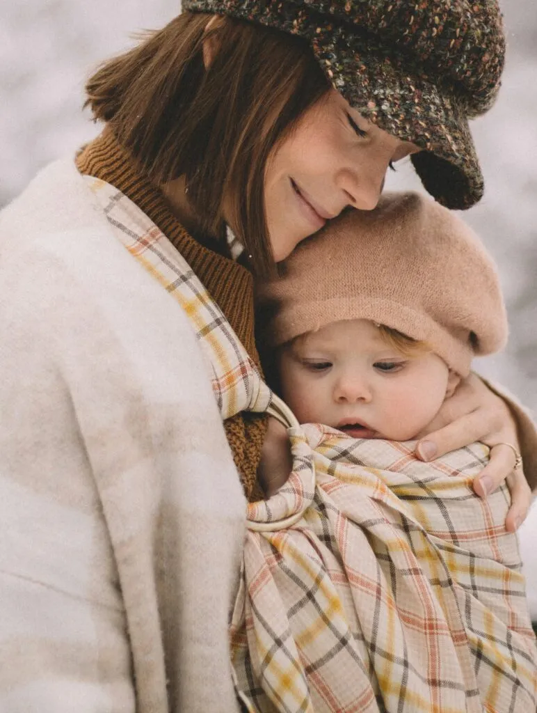 Parent holding a baby in a baby carrier, demonstrating babywearing.
